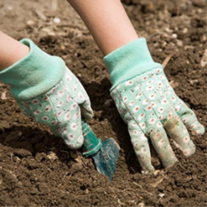 Mensch mit Gartenhandschuhen, mit einem Blumenmotiv, gräbt in der Erde mit einer Schaufel.